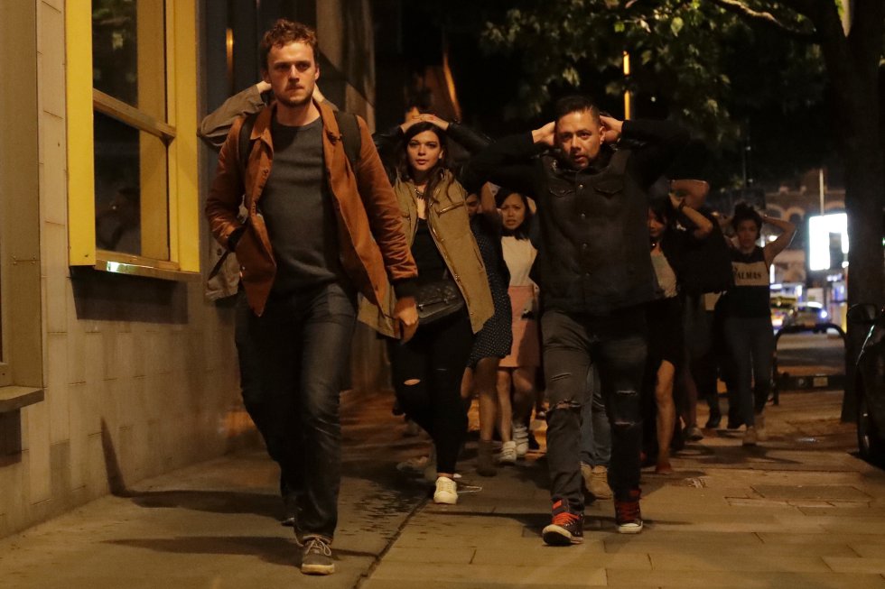 Personas con las manos en la cabeza salen de dentro del cordón policial después del ataque en Londres.