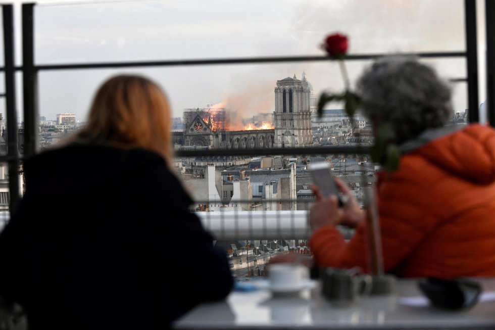 Duas pessoas observam o incêndio em Notre-Dame de um café parisiense. 