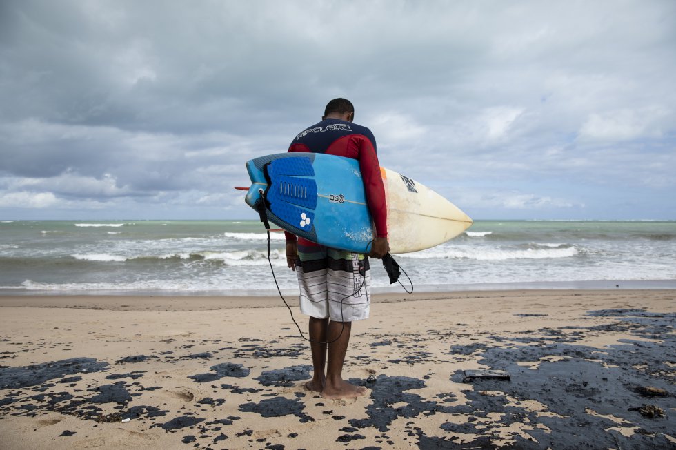 O surfista Edson “Parafina” observa desolado a condição da praia contaminada pelo óleo. Acostumados a surfar nas praias da região norte de Alagoas, os esportistas estão impossibilitados de entrar no mar devido ao vazamento.