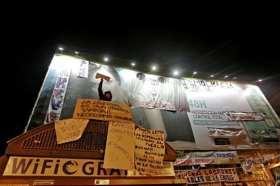 El cartel publicitario que cubre uno de los edificios de la Puerta del Sol se va cubriendo poco a poco con pancartas con eslóganes reivindicativos del Movimiento 15-M.