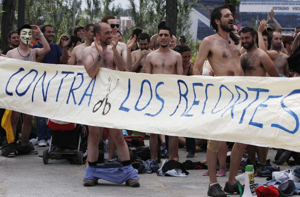Un grupo de manifestantes se desnuda tras una pancarta que dice 'Contra los recortes' durante la marcha de protesta que conmemora el aniversario del 15-M en Madrid.