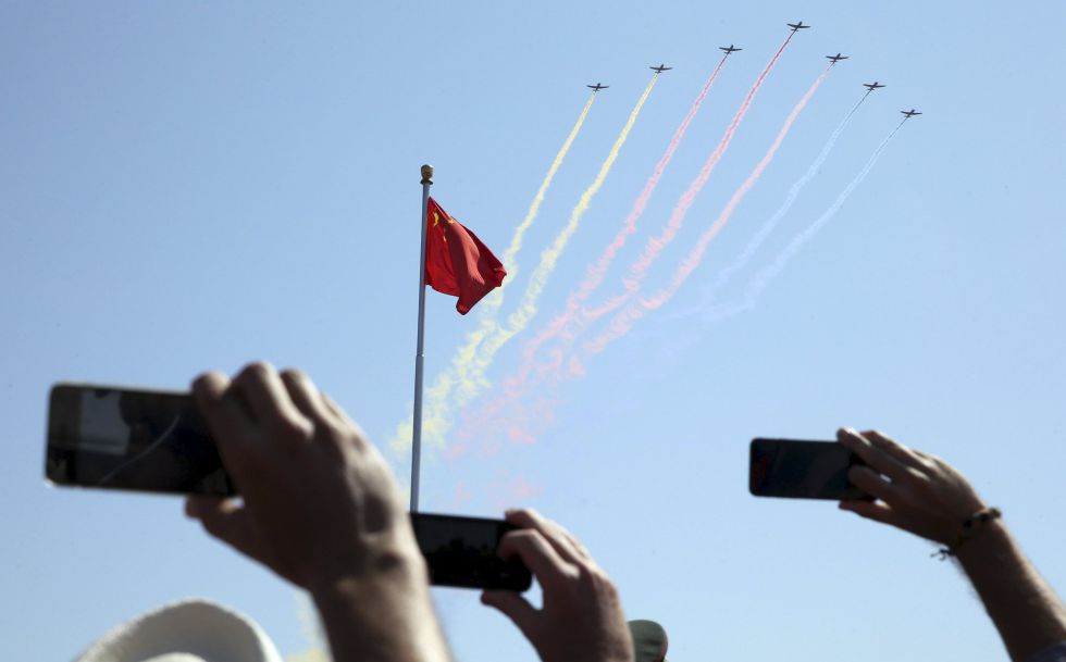 Asistentes al desfile fotografían con sus teléfonos móviles a los aviones de combate que sobrevuelan la plaza de Tiananmen, en Pekín.
