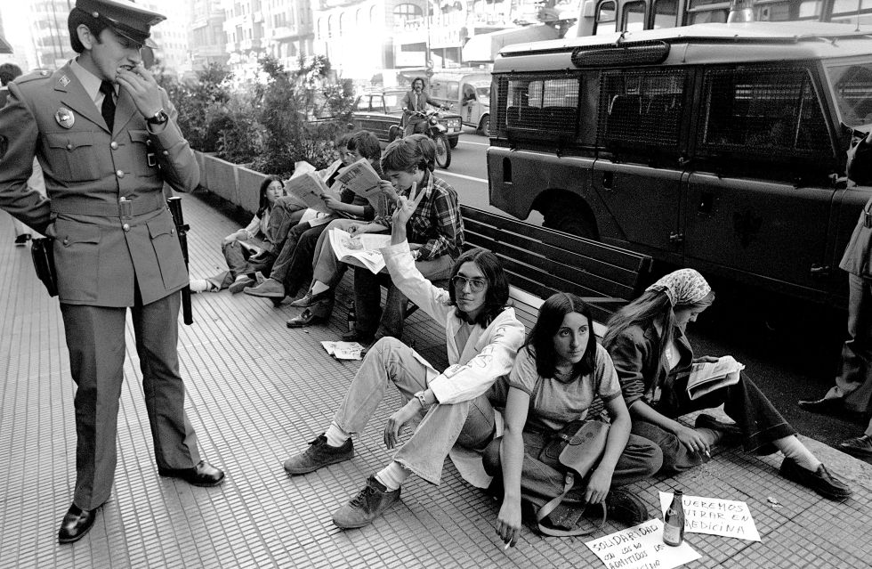 8 de octubre de 1976. Un agente de policía mira a un grupo de estudiantes encadenados a un banco de la Gran Vía de Madrid, en protesta por no haber sido admitidos en la facultad de Medicina de la Universidad Complutense.