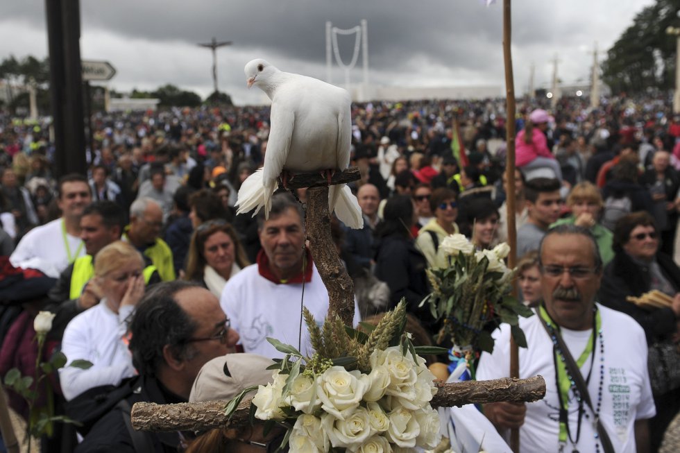 Una paloma blanca atada a un crucifijo de madera, llevada por un grupo de peregrinos a su llegada al Santuario.