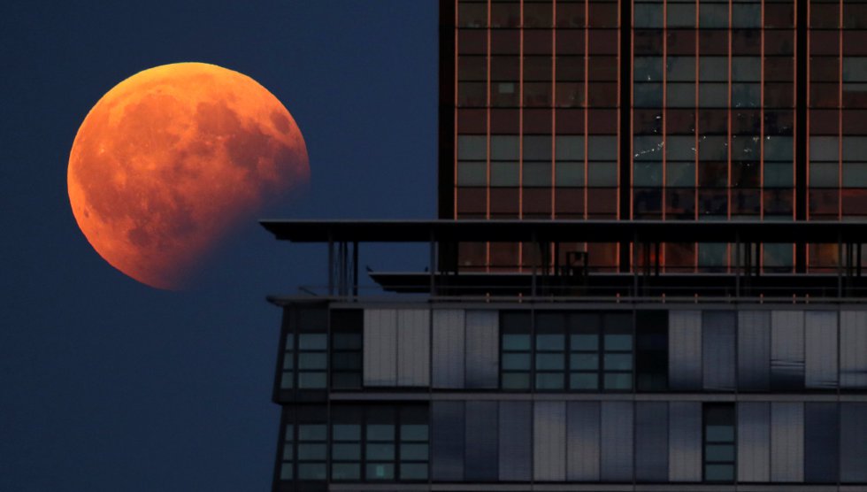 Vista del eclipse lunar parcial tras un edificio en Berlín (Alemania).