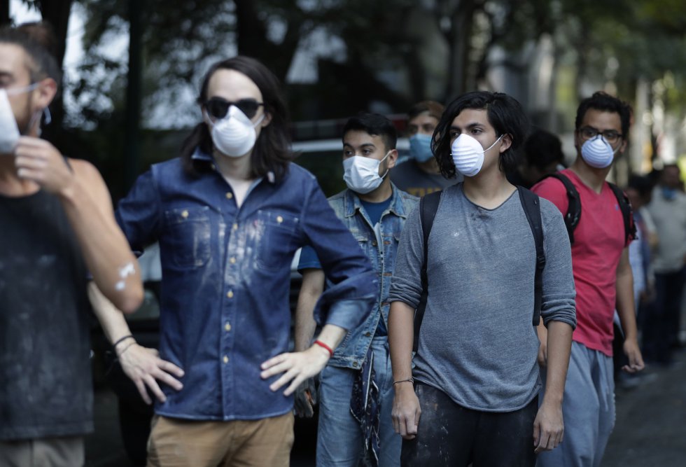 Voluntarios con máscaras esperando frente a la línea de escombros en Ciudad de México mientras los equipos de rescaten trabajan dentro de un edificio derruido por el sismo.