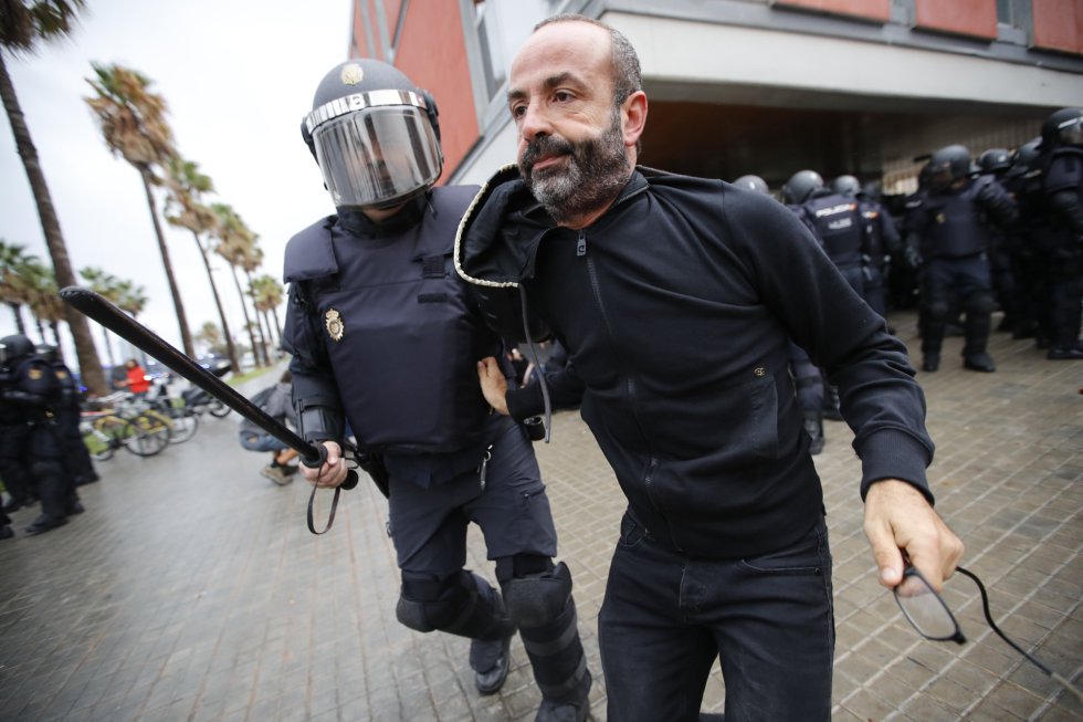 Carga policial en la escola Mediterránea de la Barceloneta (Barcelona). Un agente acompaña a un ciudadano a salir del perímetro de seguridad.