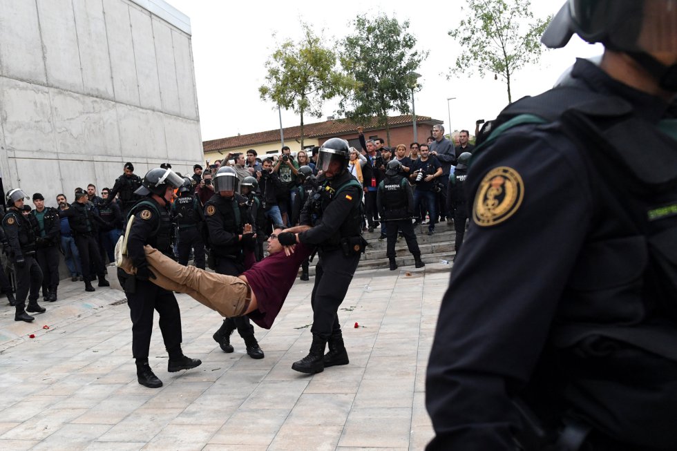 Un hombre es desalojado a la fuerza por cuerpos policiales, mientras se evita la apertura de los colegios para la votación en el referéndum independentista.