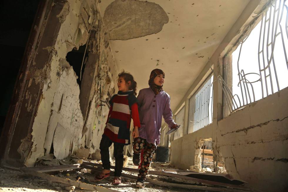 Dos niñas recorren su escuela dañada en la ciudad sitiada de Saqba (Siria).