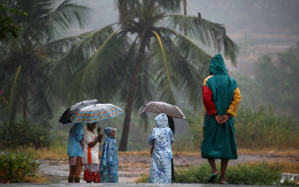 Varias personas se protegen de la lluvia con sus paraguas y chubasqueros durante una tormenta en la playa de Valenkanni, a las afueras de Bombay (India).