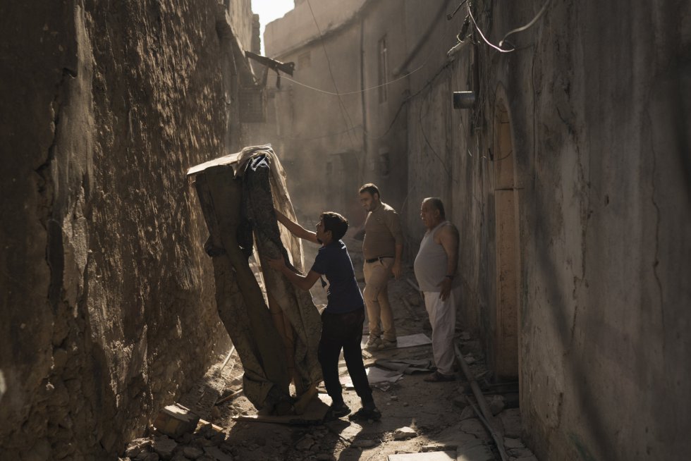 Mustafa Hansen (i), ayuda a su padre, Ahmed Mohammed (c) y a su abuelo, Mohammed Tahar, a limpiar el callejón que lleva a su casa en la Ciudad Vieja de Mosul. Al carecer de suficientes fondos del gobierno o de la comunidad internacional, los iraquíes han comenzado a reconstruir por su cuenta, absorbiendo ahorros y pidiendo prestado a amigos y familiares.