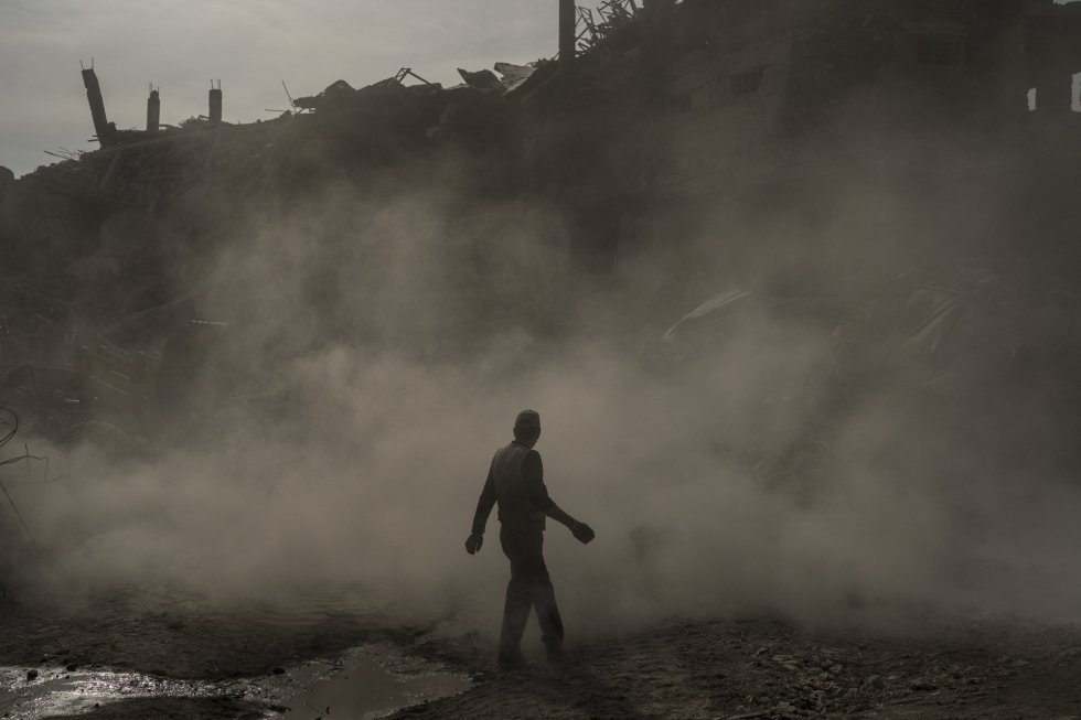 Un trabajador de la construcción camina entre una nube de polvo mientras una excavadora quita escombros de una zona de tiendas destruida en la Ciudad Vieja de Mosul.