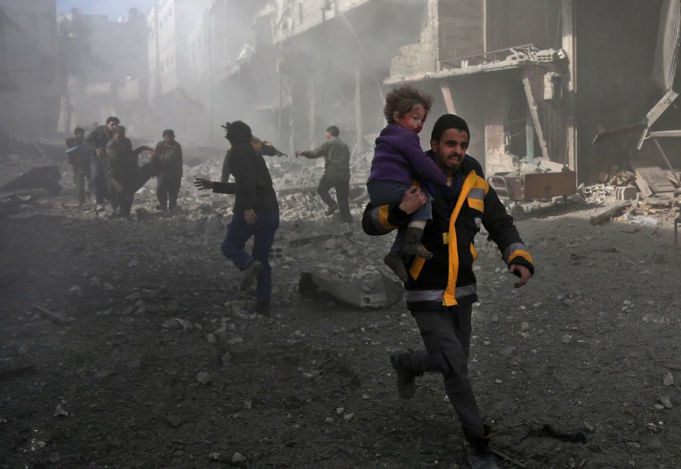 Un hombre corre con un niño en brazos entre los escombros tras un bombardeo en Hamouria (Siria), el 19 de febrero de 2018.