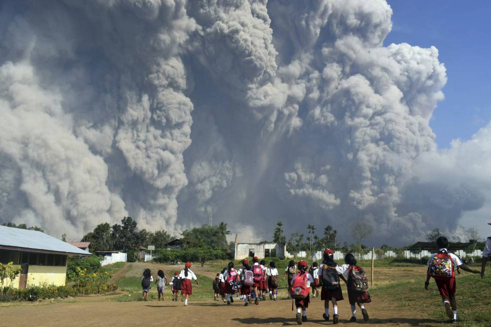 Un grupo de estudiantes camina frente a la columna de humo y ceniza provocada por la erupción del volcán Monte Sinabung en Karo (Indonesia), el 19 de febrero de 2018.