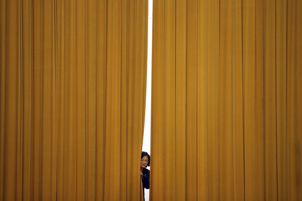 Un miembro del staff se asoma por una cortina antes de una rueda de prensa, tras la Asamblea anual del Parlamento chino en el Gran Salón del Pueblo de Pekín (China).