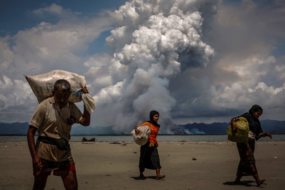 Nuvem de fumaça sobe na fronteira com Mianmar, enquanto refugiados rohingyas caminham pela costa depois de terem conseguido cruzar para Bangladesh de barco pela Baía de Bengala, em Shah Porir Dwip (Bangladesh), em 11 de setembro de 2017.