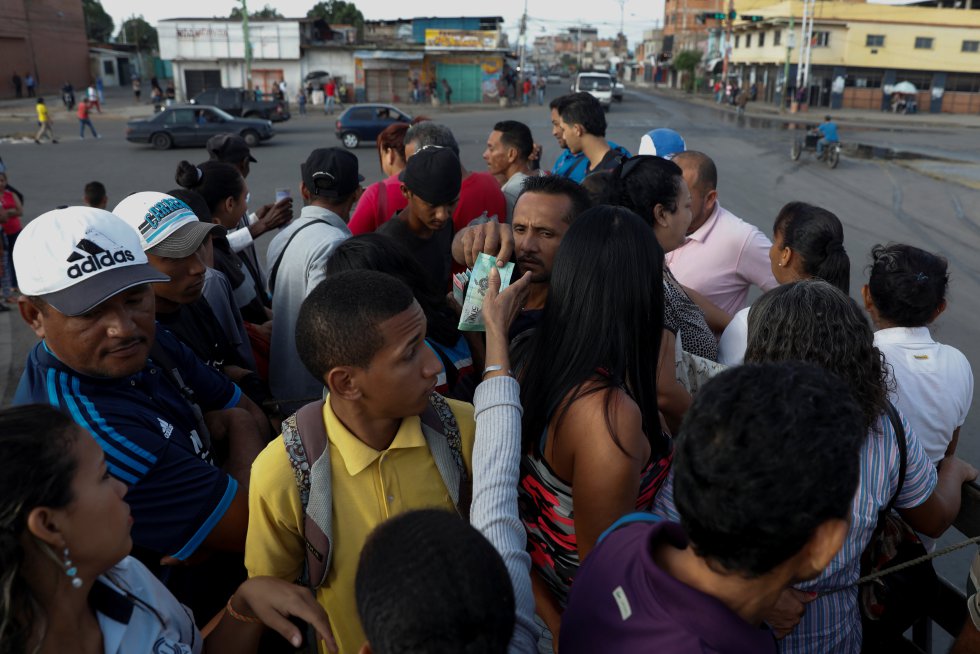 Os venezuelanos se aglomeram para subir a um destes veículos que funcionam tanto na capital, Caracas, como em outras grandes cidades do país. Um passageiro paga por um bilhete em um caminhão de carga utilizado como transporte em Valência, no Estado de Carabobo (centro), no dia 12 de julho.