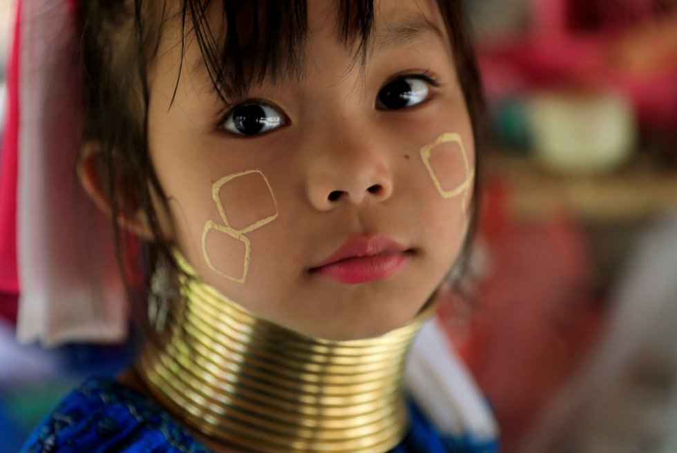 Una niña de etnia Kayan, también conocida como una niña de cuello largo, se sienta en la tienda de recuerdos de sus padres en el pueblo de Kayan (Tailandia).  rnrn