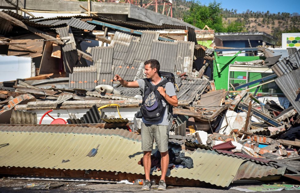 Un turista trata de hacer autoestop frente a unos edificios derrumbados en Pemenang, Lombok, el 6 de agosto de 2018. 