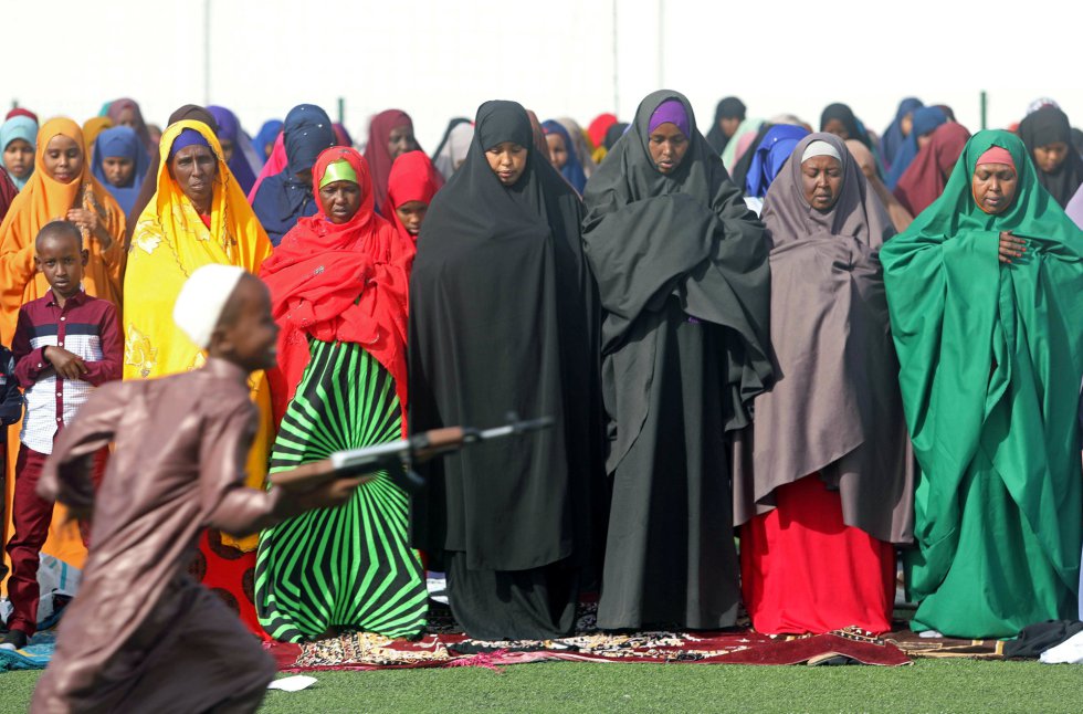 Un niño corre con un arma de juguete frente a un grupo de mujeres rezando, el 21 de agosto de 2018, en Mogadishu, Somalia.