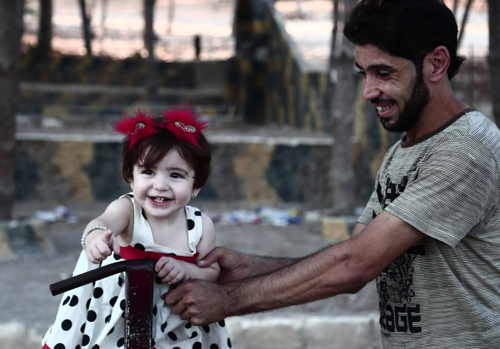 Un hombre juega con una niña en el segundo día del 'Eid el-Adha' o fiesta del sacrificio, la mayor festividad de la comunidad musulmana, en un parque de la ciudad siria de Afrin, el 22 de agosto de 2018. Desplazadas de sus hogares en la Ghouta Oriental de Siria, las familias buscaron refugio en casas abandonadas en la ciudad kurda de Afrin a principios de este año.