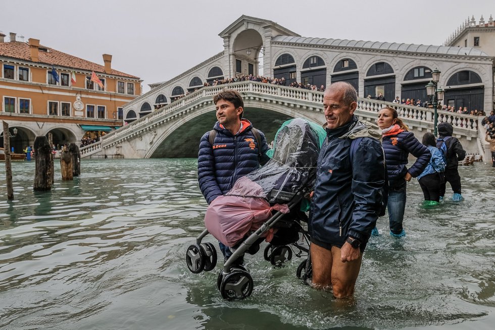 Dos turistas elevan un carrito para cruzar las calles inundadas en Venecia (Italia), este lunes. Al fondo el Puente Rialto, que cruza el Gran Canal.
