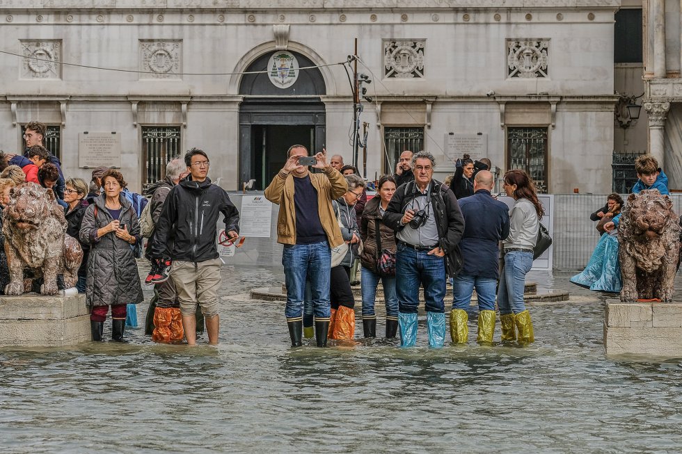 Un grupo de turistas toman fotografías y observan la plaza de San Marcos inundad por la subida del nivel del agua.