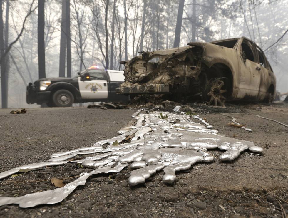 Un coche de policía pasa el viernes pasado junto a un vehículo chamuscado por el incendio que desde hace varios días asola Paradise, en California (EE UU).