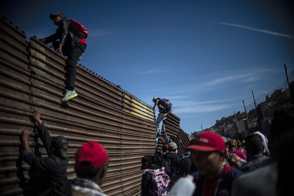 Un grupo de migrantes centroamericanos, en su mayoría hondureños, trepan la frontera entre México y Estados Unidos, cerca del cruce de El Chaparral, en Tijuana.