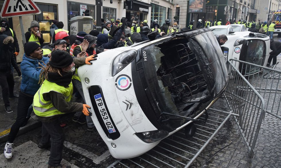 Varios manifestantes vuelcan algunos vehículos, durante la protesta de los 'chalecos amarillos' contra el aumento del precio de los carburantes, cerca de los Campos Elíseos en París.