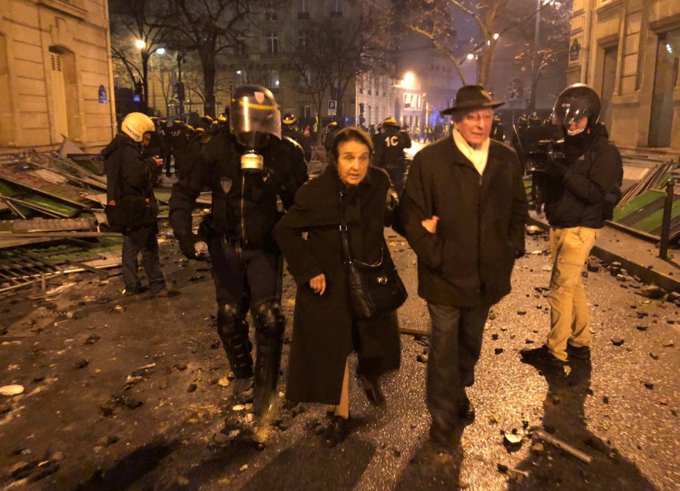 La policía antidisturbios francesa acompaña a una pareja de ancianos, para que cruce una calle devastada por los enfrentamientos.