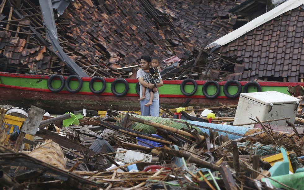Un hombre con un niño en brazos obseva los daños en una aldea devastada por el tsunami en Sumur, Indonesia.