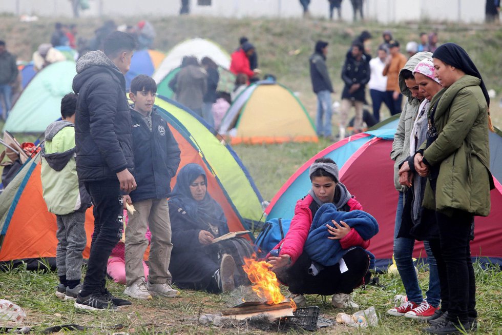 Varias personas se calientan en torno a una hoguera, este viernes en el campo de refugiados del pueblo de Diavatá-