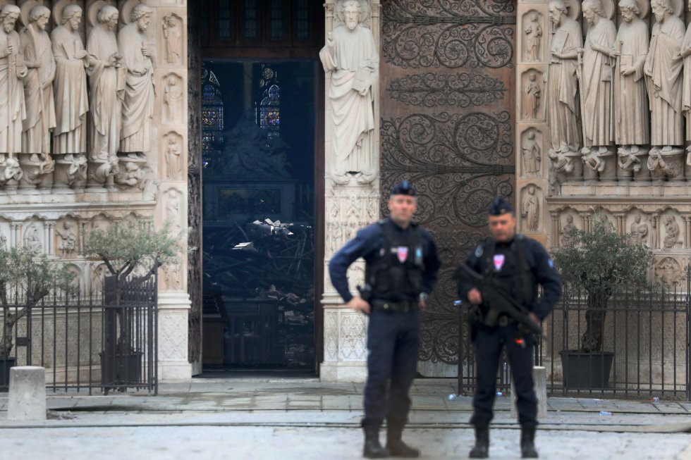 Dos policías vigilan junto a la catedral de Notre Dame en cuyo interior se puede ver una pila de escombros, este martes, en París (Francia). 