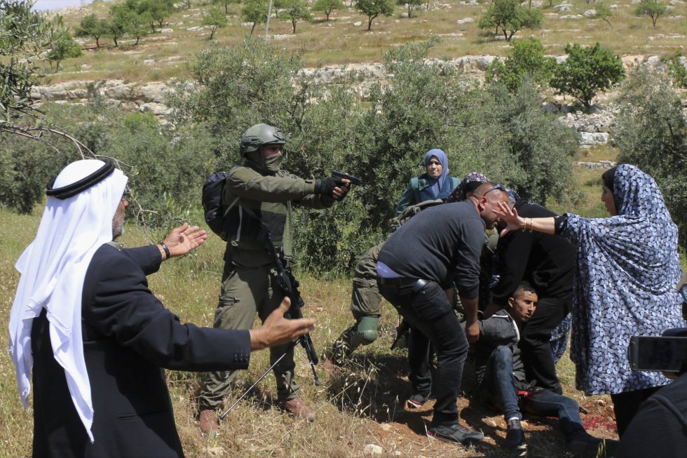 Un soldado israelí apunta con su pistola a un grupo de palestinos que se reúnen alrededor del adolescente de 15 años Osama Hajahjeh, herido tras los disparos de las fuerzas israelíes, en la aldea de Tekoa, en Cisjordania.