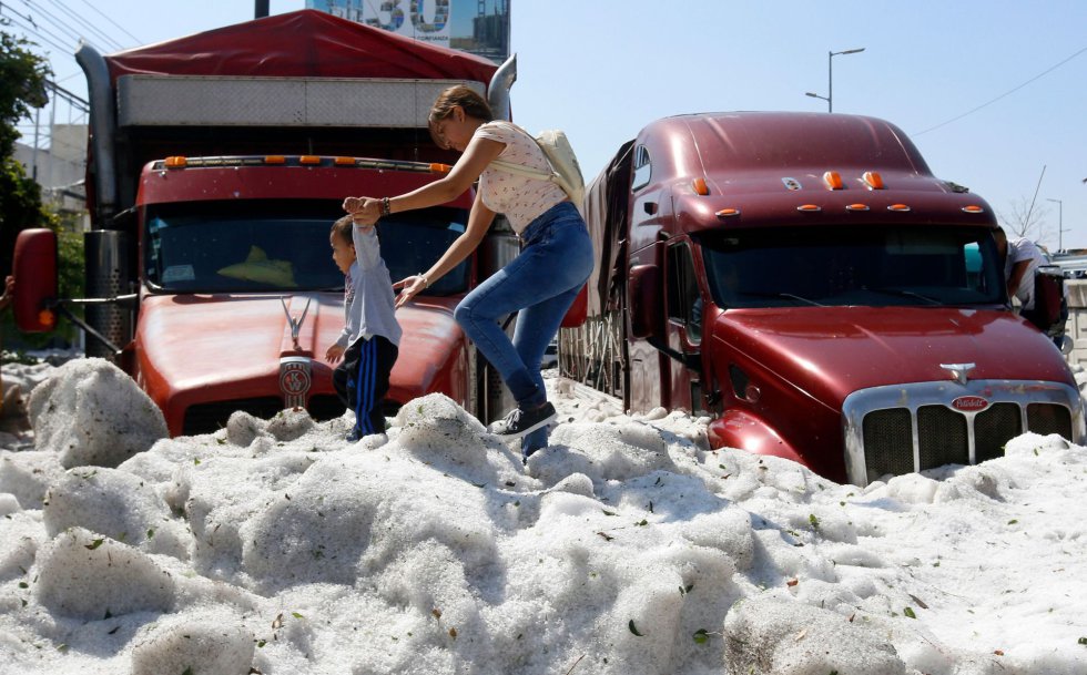 El granizo afectó a decenas de vehículos en Guadalajara, capital del estado de Jalisco, y dejó sepultados numerosos coches. En la imagen, una mujer camina junto a su hijo sobre una montaña de granizo.