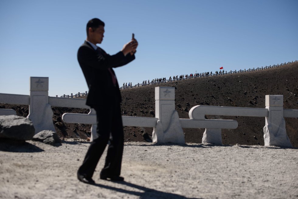 Um segurança tira uma foto enquanto um grupo de estudantes norte-coreanos marcha para o topo do Monte Baekdu, perto de Samjiyŏn. Todos os anos, 100.000 norte-coreanos ou mais visitam o Monte Baekdu em excursões ao campo, montanhas e locais revolucionários próximos, onde as relíquias são preservadas.