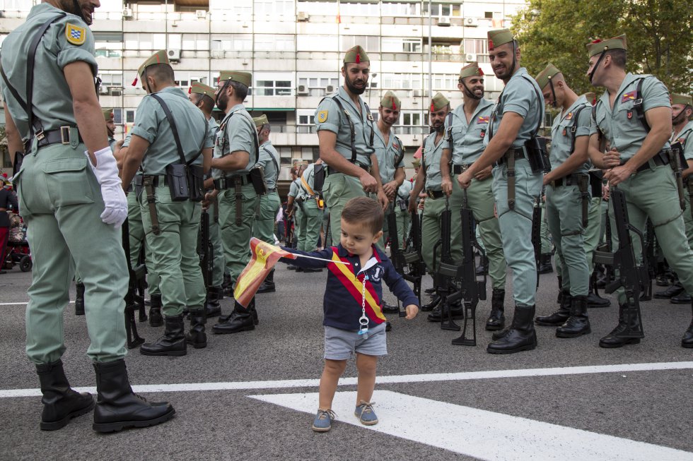 Un niño ondea una bandera de España entre legionarios antes del desfile.