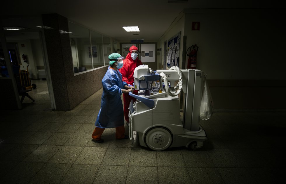 Dos sanitarios trasladan un equipo portátil de radiología por una de las plantas destinadas a UCI del hospital. Los equipos de rediodiagnóstico son fundamentales para el tratamiento de la enfermedad ya que permiten evaluar el daño pulmonar en pacientesgraves, que no pueden ser trasladados fuera de la unidad de intensivos.