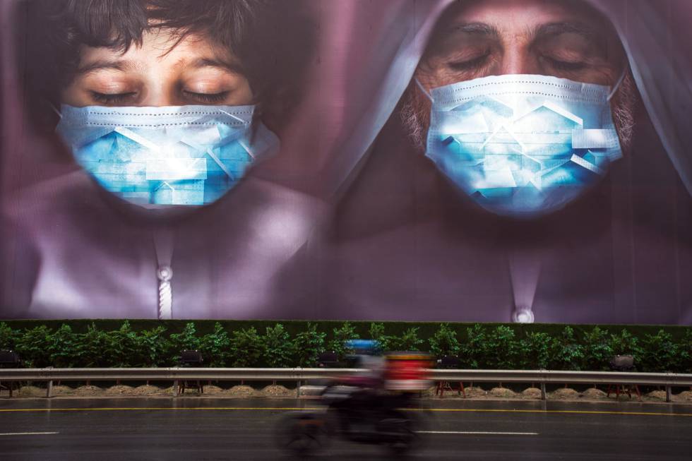 Un repartidor pasa junto a una valla publicitaria instando a las personas a utilizar mascarillas en Dubái (Emiratos Árabes).