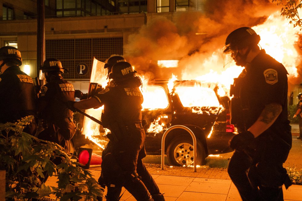 La muerte de George Floyd, un hombre negro, a causa de una brutal acción de un policía blanco de Minneapolis, ha encendido por quinto día consecutivo la mecha del resentimiento racial en el país. En la imagen, un grupo de policías antidisturbios pasa delante de un coche ardiendo en Minneapolis.