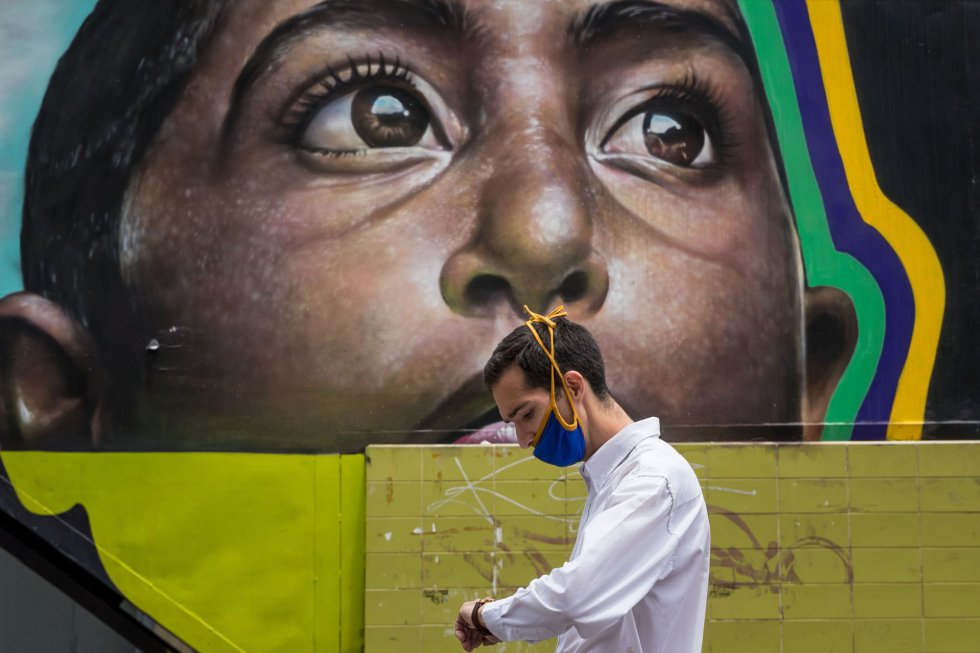 Un hombre con una mascarilla camina frente a un mural, en Caracas (Venezuela). Caracas y el cercano estado de Miranda entrarán de nuevo en una cuarentena radical para frenar los contagios del nuevo coronavirus, solo después de dos días de una flexibilización que se mantiene en otras regiones, informó la vicepresidenta de Venezuela, Delcy Rodríguez.