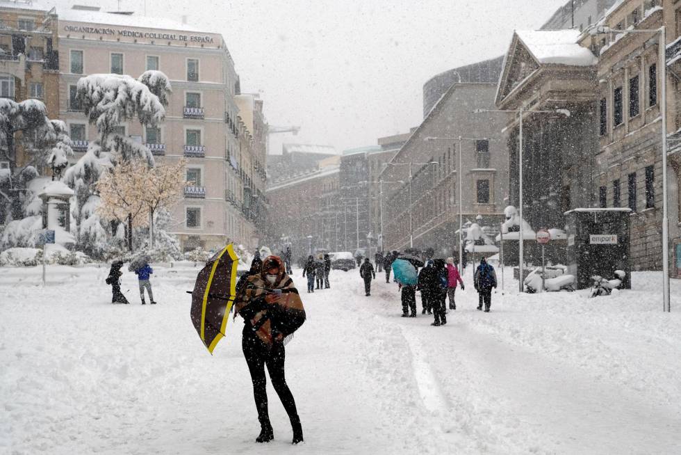 Una mujer se protege de la nieve (en primer plano) en la carrera de San Jerónimo de Madrid, este sábado. A mano derecha, el Congreso de los Diputados.