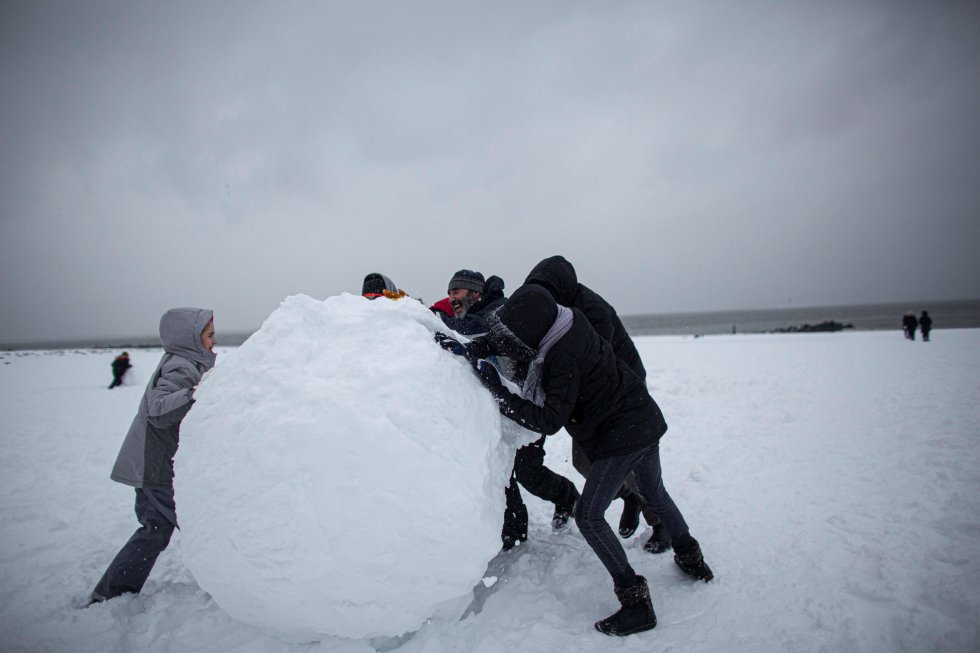 Varias personas hacen una bola de nieve gigante durante una tormenta invernal en Brighton Beach.