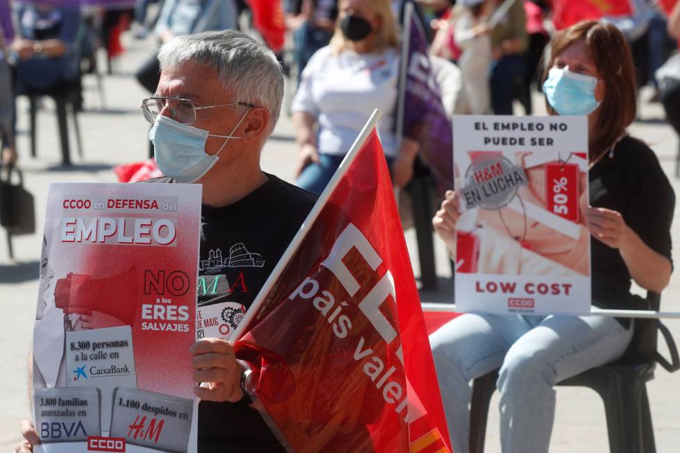 Dois participantes exibem faixas contra cortes e dispensas durante o comício do Primeiro de Maio no centro de Valência.