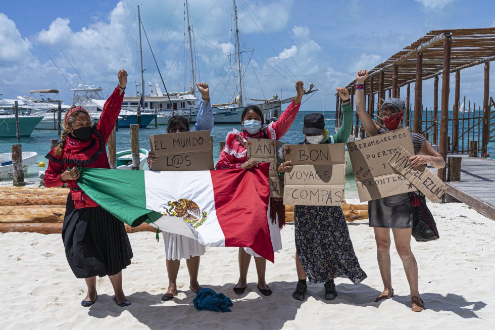 Activistas otomíes y francesas sostienen pancartas con mensajes de apoyo para el grupo de zapatistas antes de su partida del puerto de Isla Mujeres, en Quintana Roo.