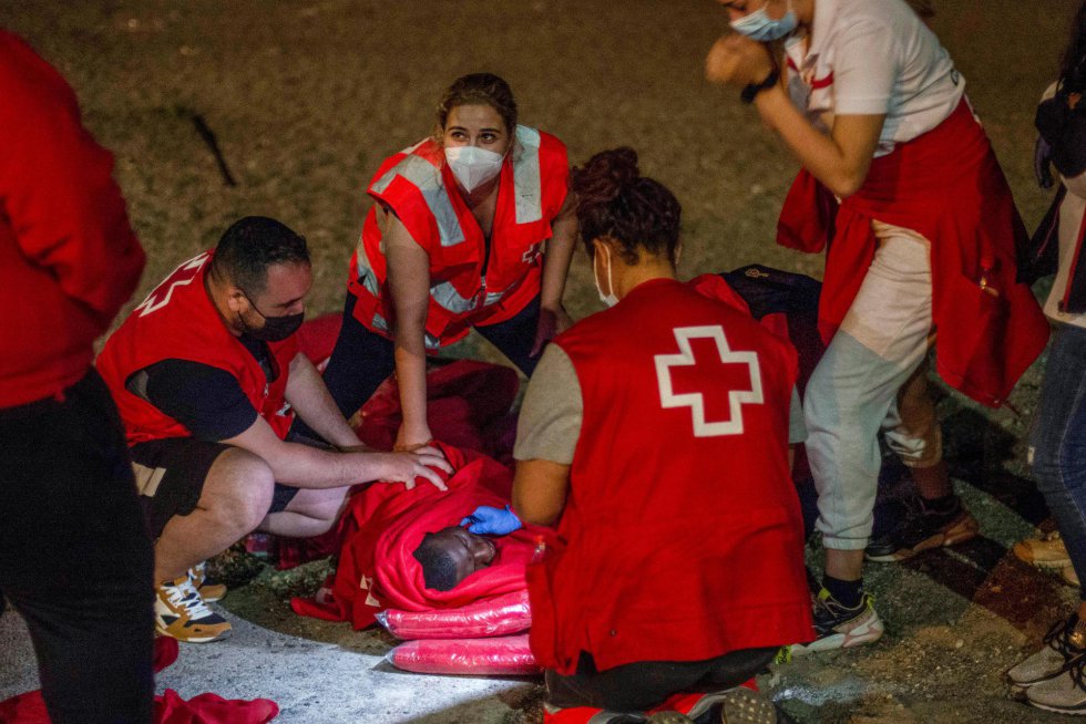 Efectivos de la Cruz Roja atienden a un migrante con signos de hipotermia en la playa del Tarajal. 106 marroquíes, entre ellos una mujer embarazada, han tenido que ser atendidos en las últimas horas en el hospital universitario y en otros centros sanitarios de la ciudad autónoma.