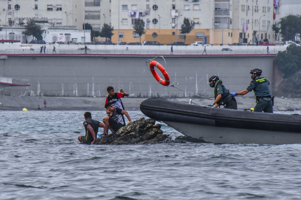 Agentes de la Guardia Civil tratan de rescatar a varios menores que se han subido a una roca en una zona cercana a la playa del Tarajal. 