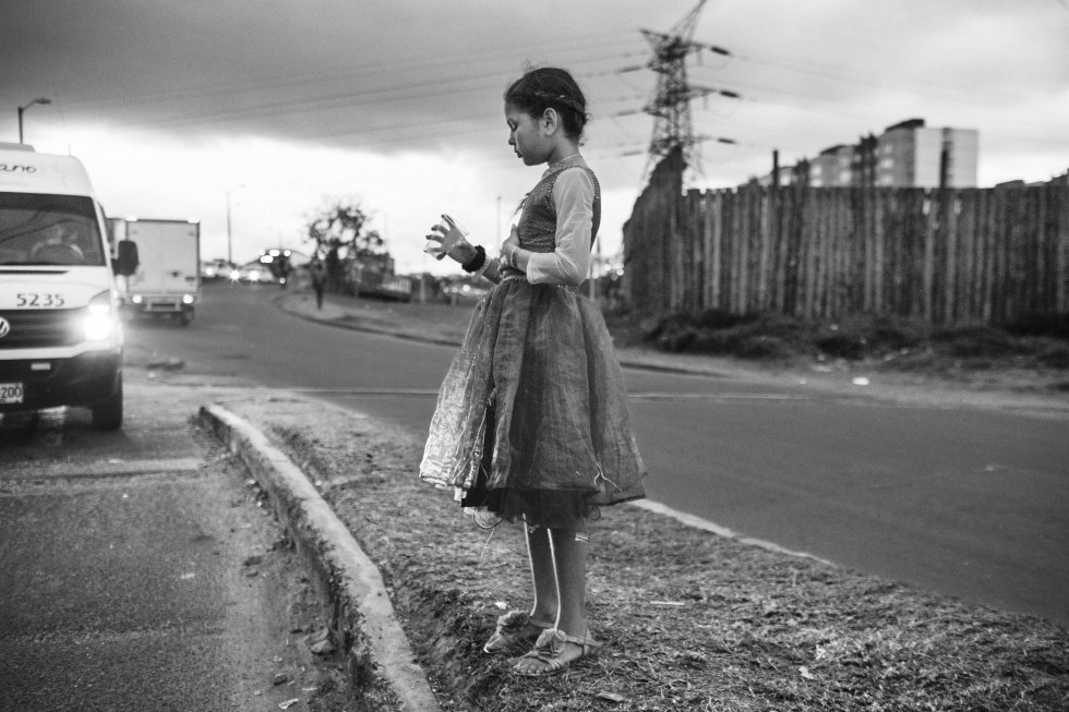 En mitad de una autopista en las calles de Bogotá, capital colombiana, una niña sostiene un vaso de plástico.rn