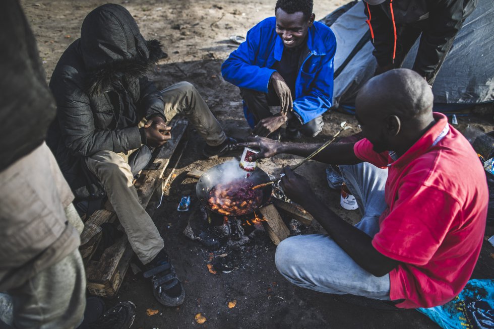 Varios inmigrantes calientan una lata de comida preparada en el campamento situado en el límite entre Calais y el municipio de Marck.